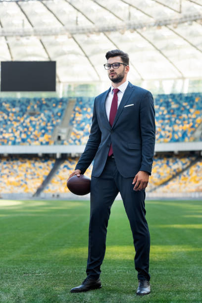 young businessman in suit and glasses with rugby ball at stadium